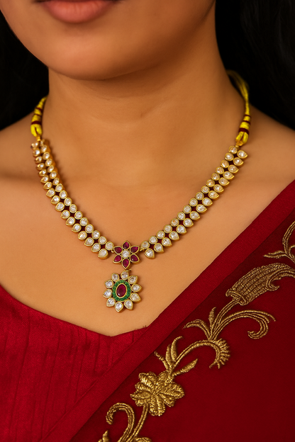 Pearl necklace with floral pendant on a person wearing a red saree with gold patterns.